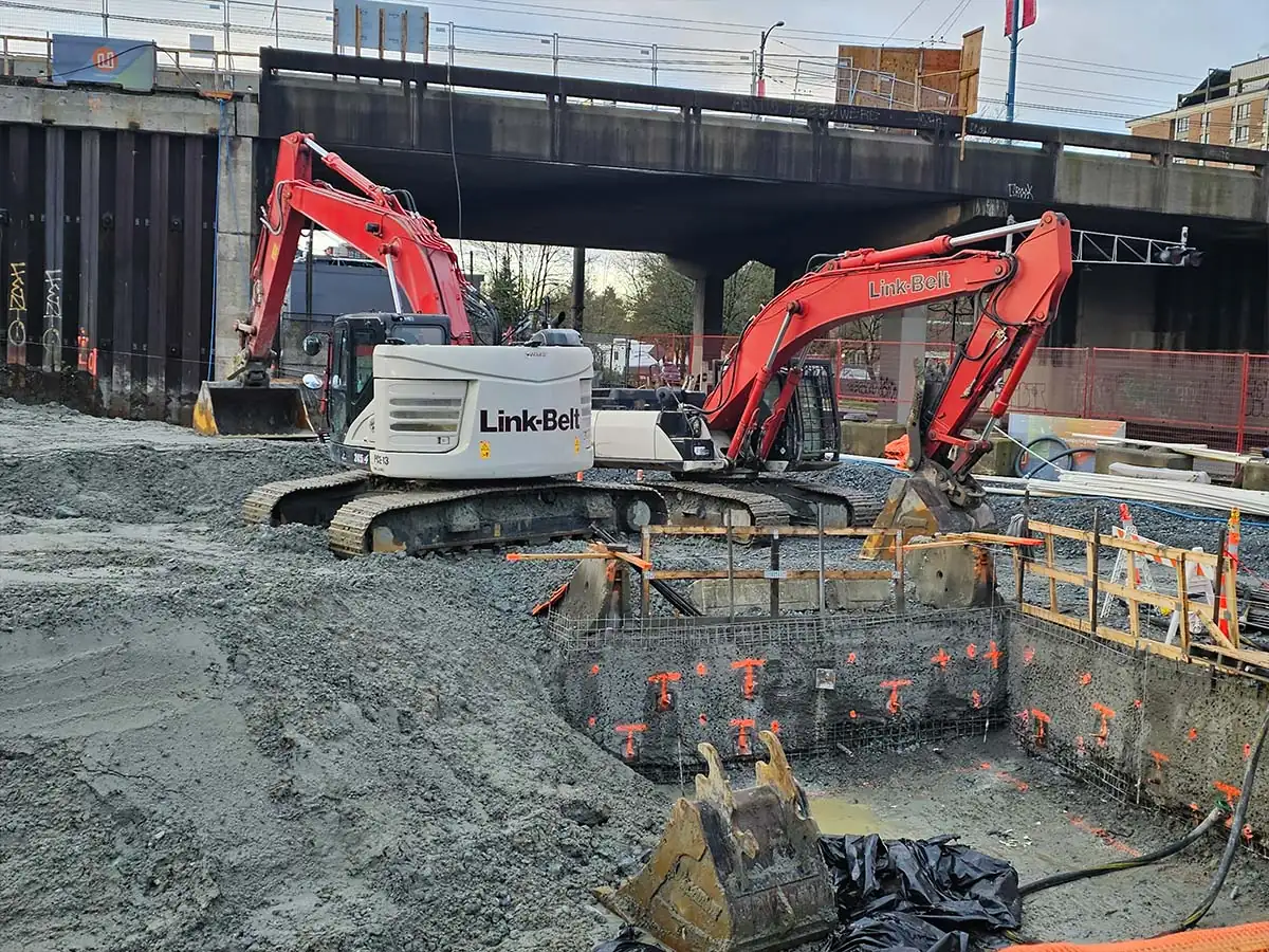 Two PCE excavators in a commercial excavation beside an elevated guideway