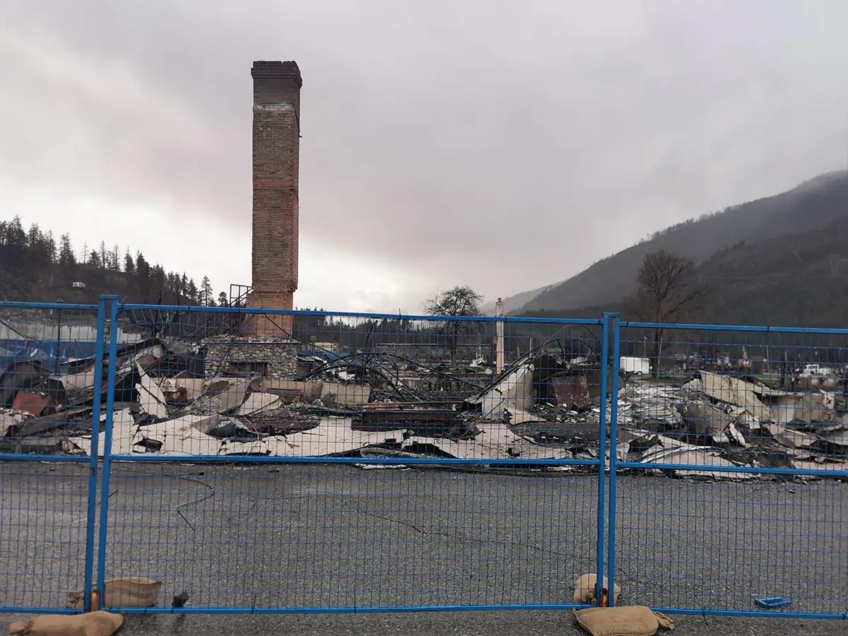 Burned-out lots and a standing chimney behind site fencing in Lytton