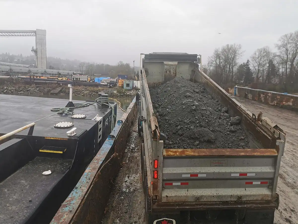 Dump truck tipping beside the loaded barge