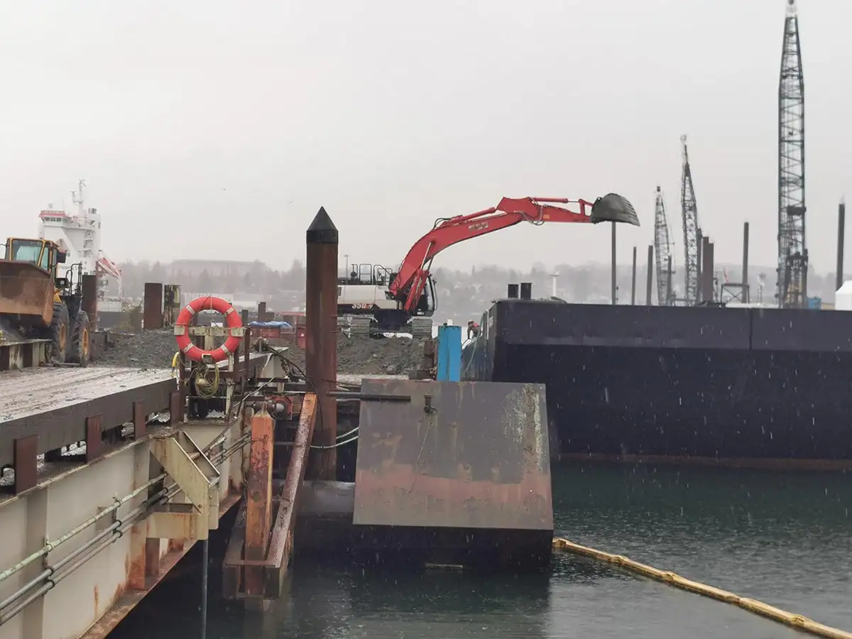 Excavator at the end of the dock beside moored barges