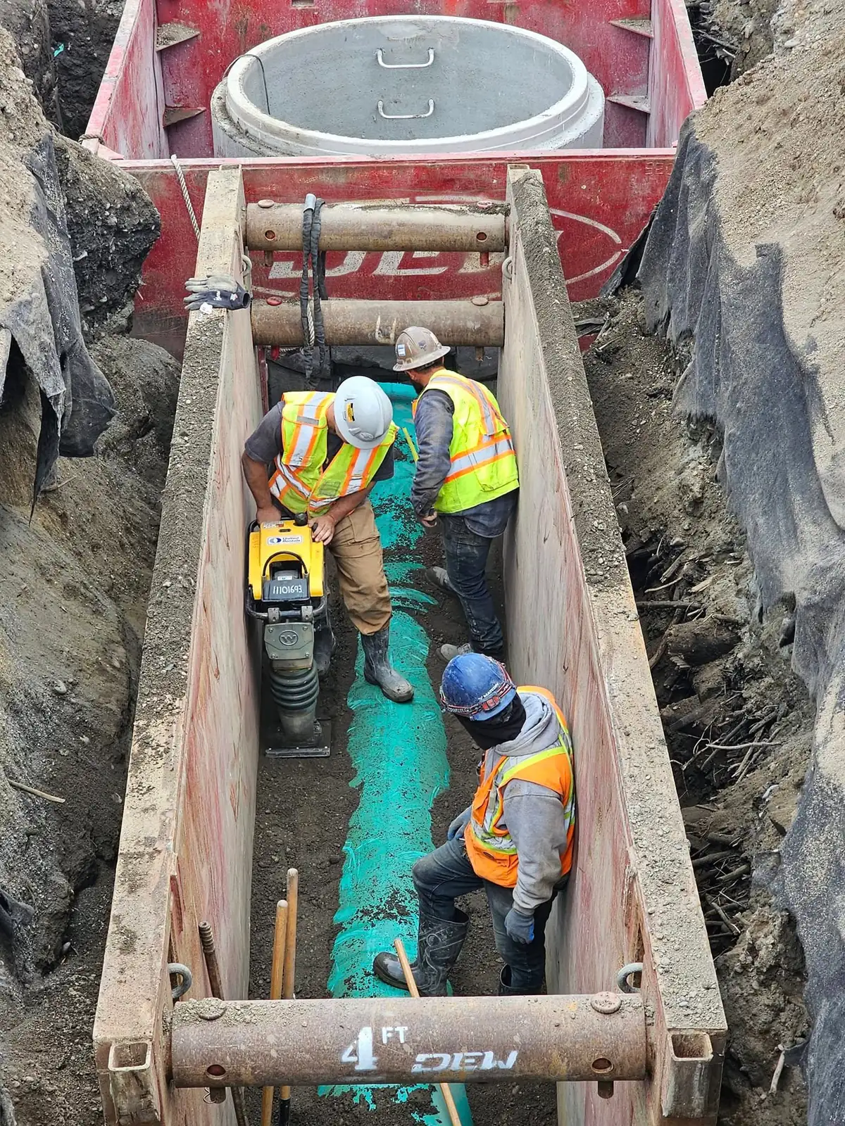 Crew compacting around new pipe inside a trench box